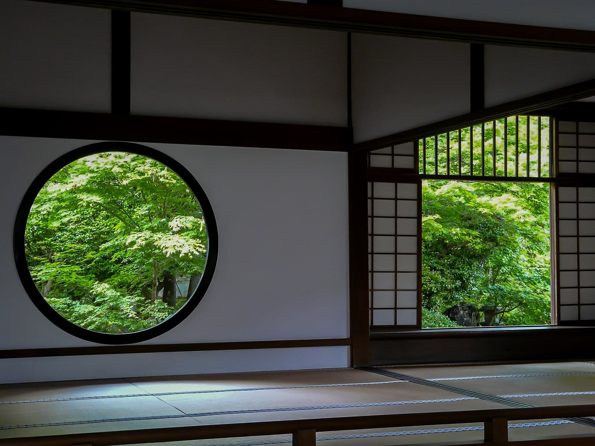 Traditional Japanese room with a circular window framing lush garden greenery — the quiet view from a solo ryokan room