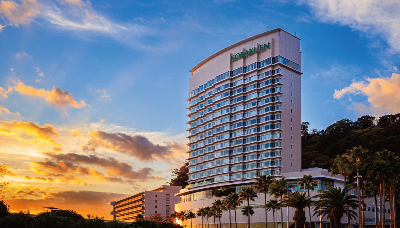 Atami Korakuen Hotel high-rise exterior at sunset above Atami Onsen bay with palm trees