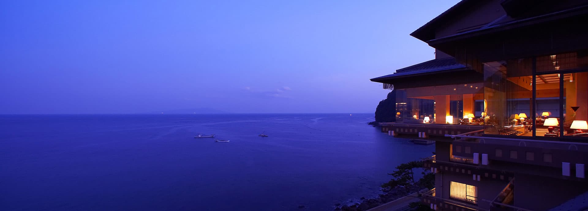 Bousui ryokan in Hokkawa Onsen, Izu, at dusk with a lit ocean-view lounge overlooking the deep-blue Sagami Bay