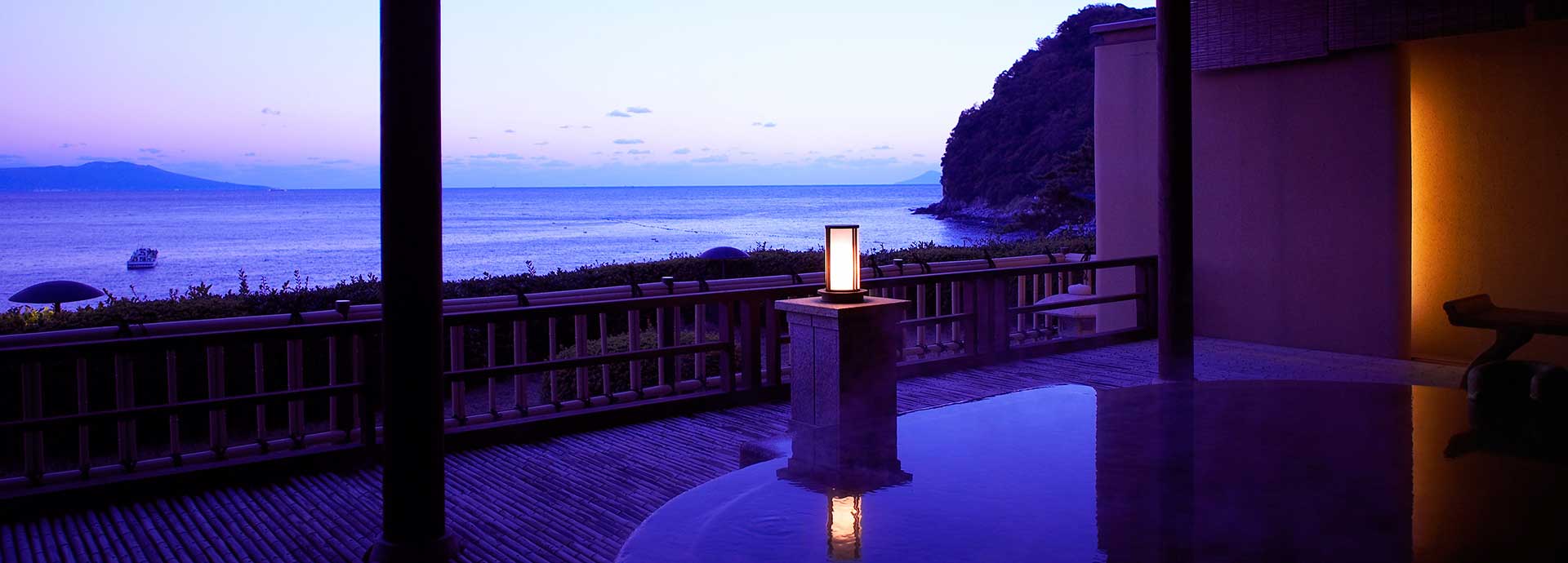 Open-air rotenburo onsen bath at Bousui glowing at dusk with a stone lantern and a sweeping view over the sea