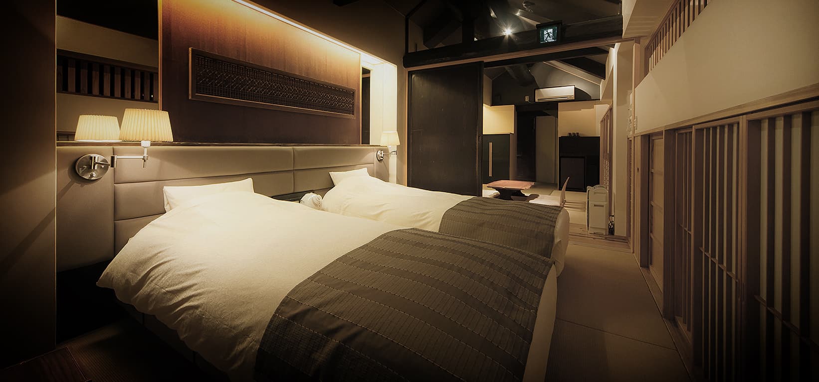 Atmospheric twin-bed villa bedroom with dark timber beams and warm lighting at CHAHARU Hanare Dogo Yumekura in Dogo Onsen