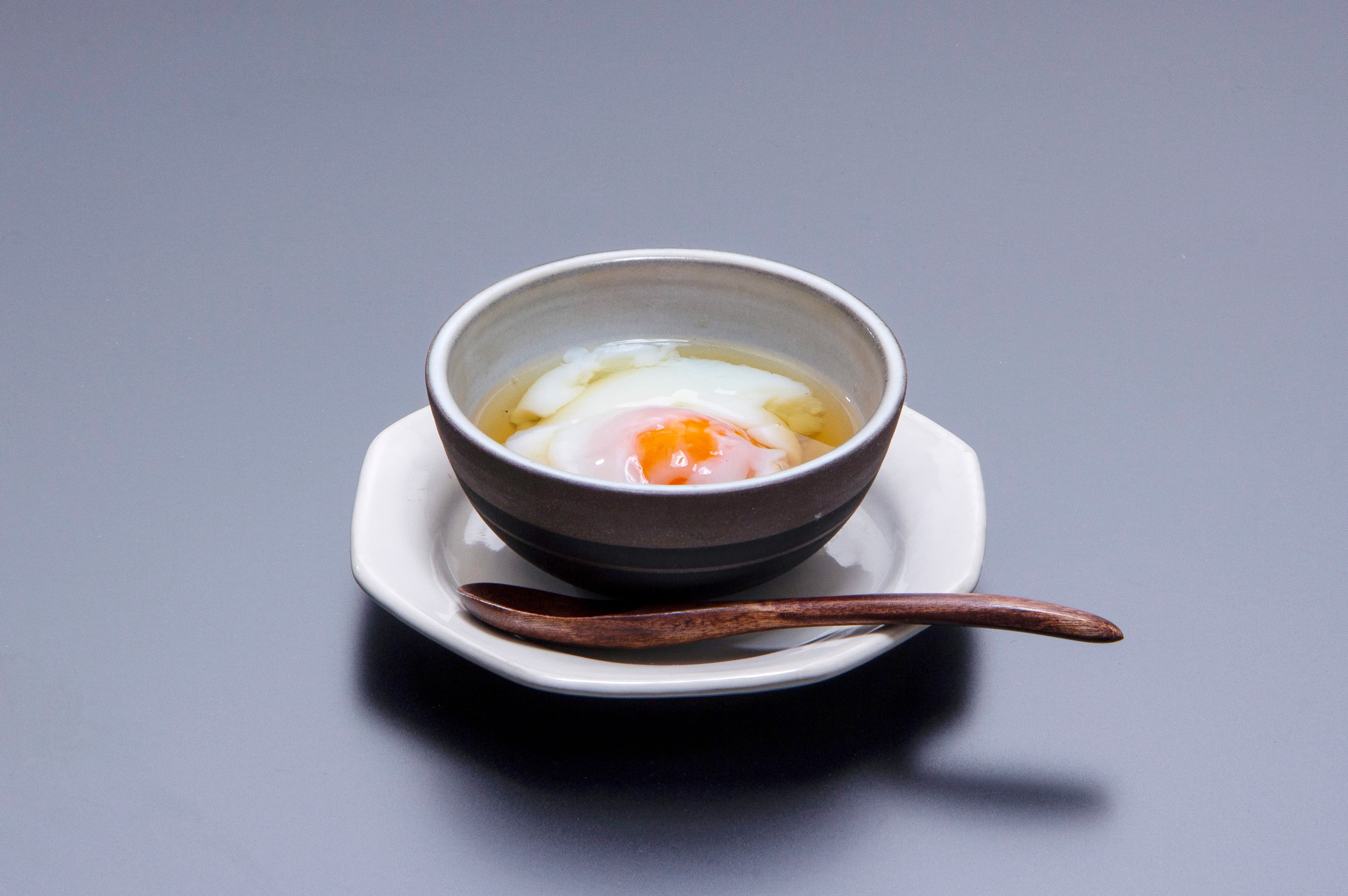 Soft-cooked onsen egg in dashi served in a ceramic bowl with wooden spoon at Yujin Chiyonoyu