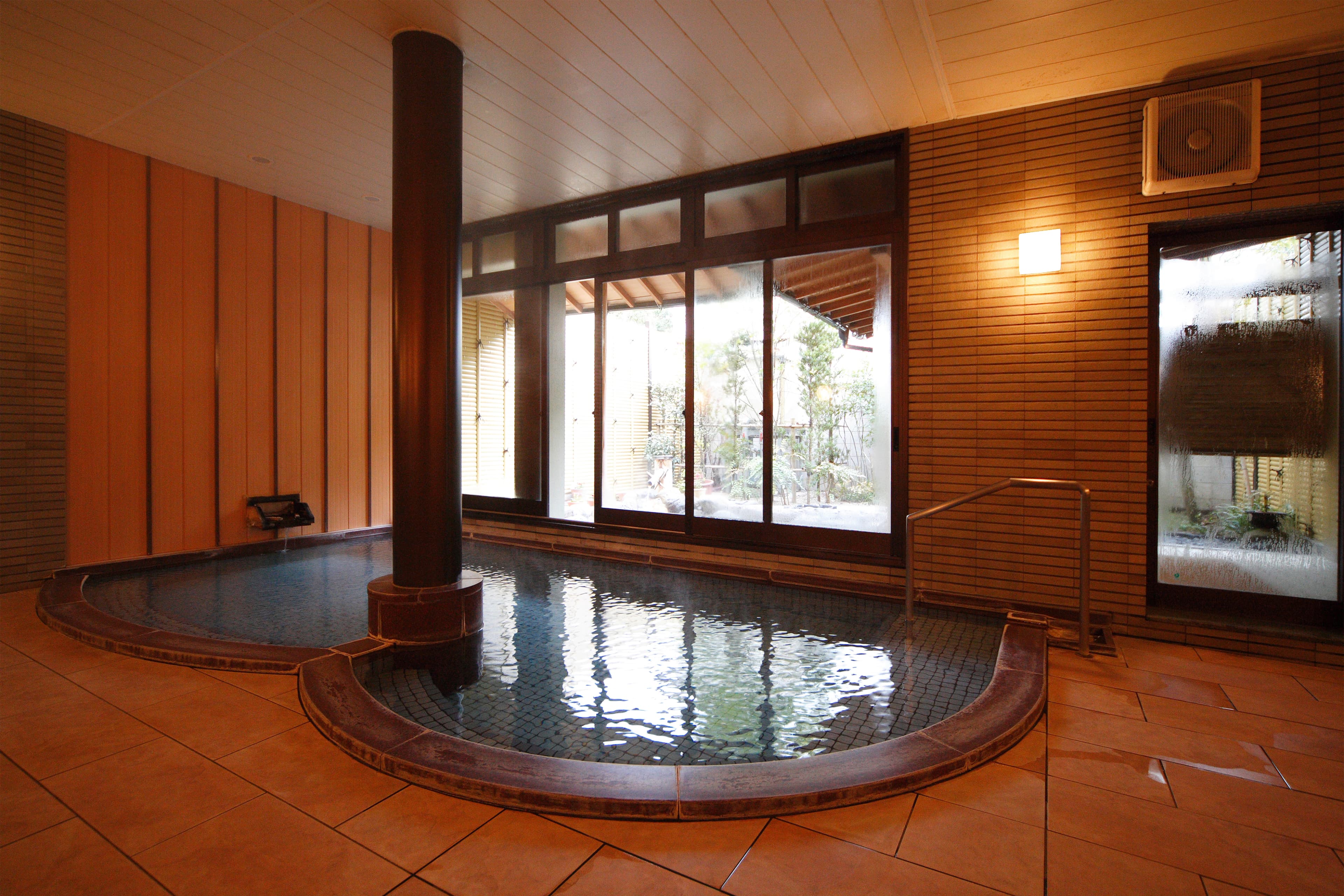 Indoor stone bath with wood-paneled walls and garden-view windows at Yujin Chiyonoyu, Tamatsukuri Onsen