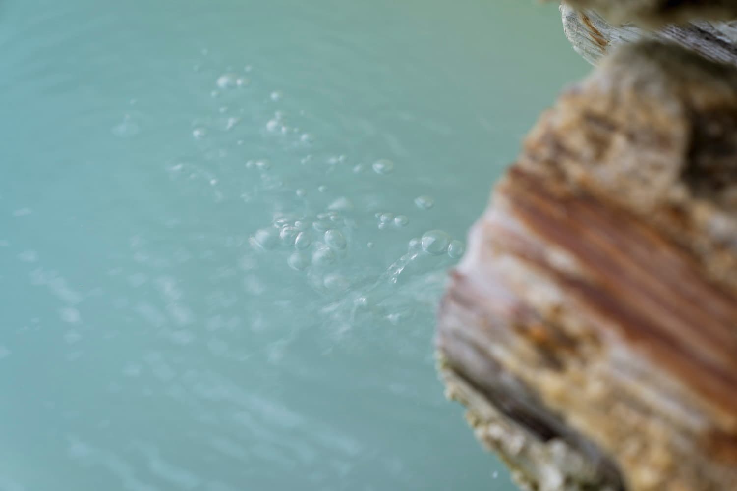 Close-up of pale milky-blue sulfur spring water bubbling beside a mineral-crusted rock at Shirahone Ebisuya