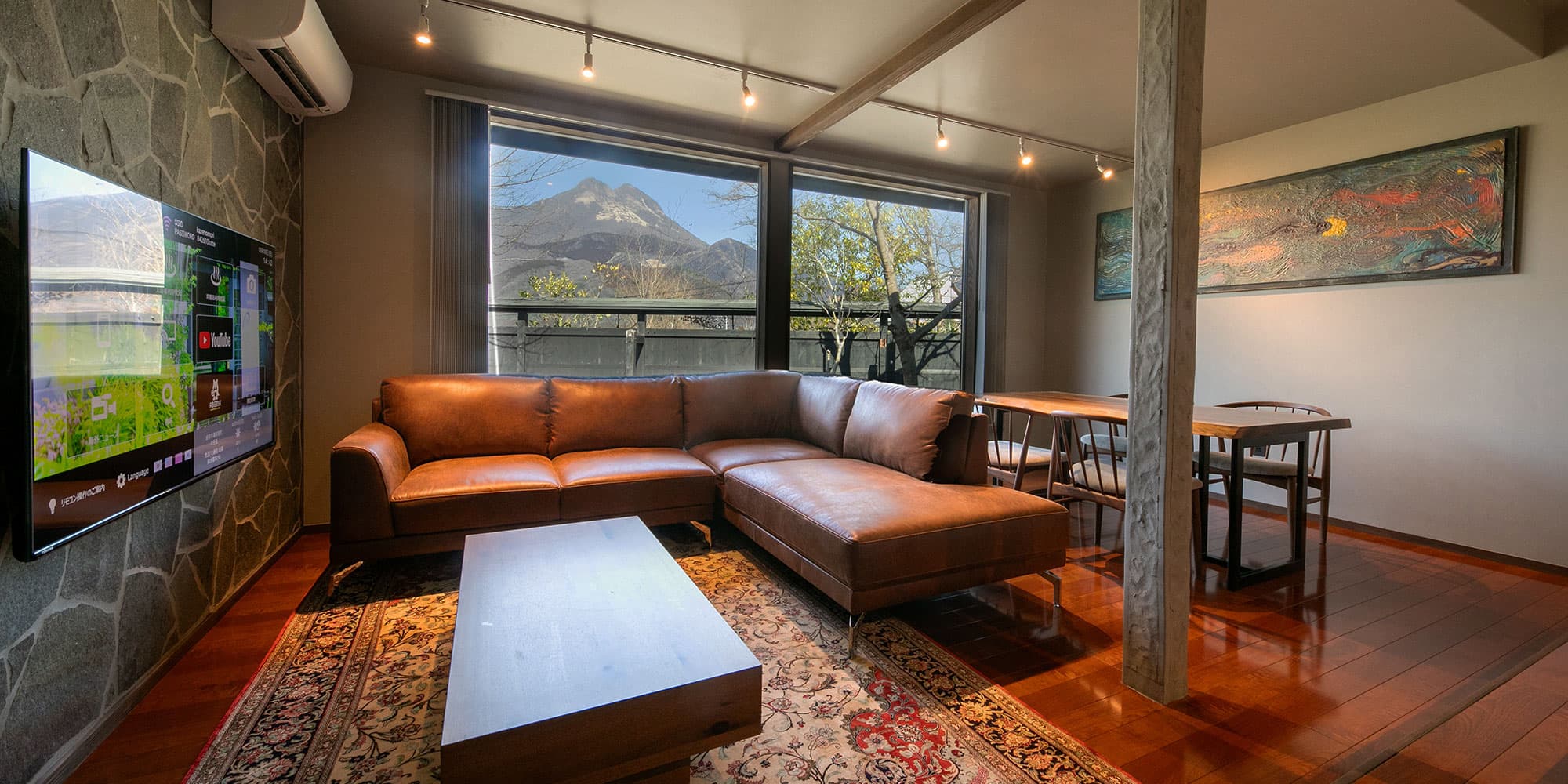 Guest suite living room with leather sofa and a Mount Yufu view through floor-to-ceiling windows at Kazenomori