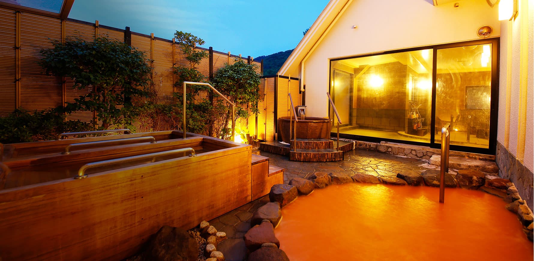 Miyukiso Hanamusubi open-air rotenburo bath filled with Arima's reddish-brown kinsen water, glowing at dusk beside a bamboo fence