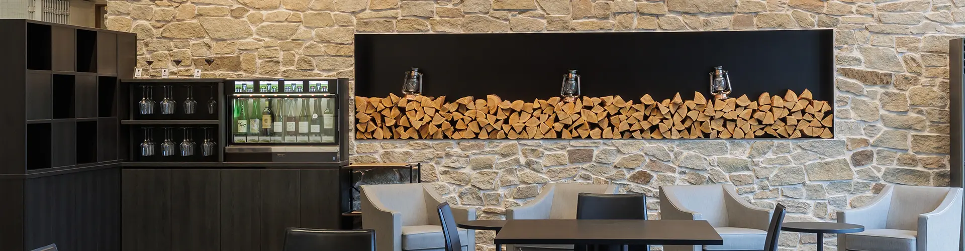 Lounge bar with stone wall, stacked firewood, hanging lanterns and a wine selection in the hotel