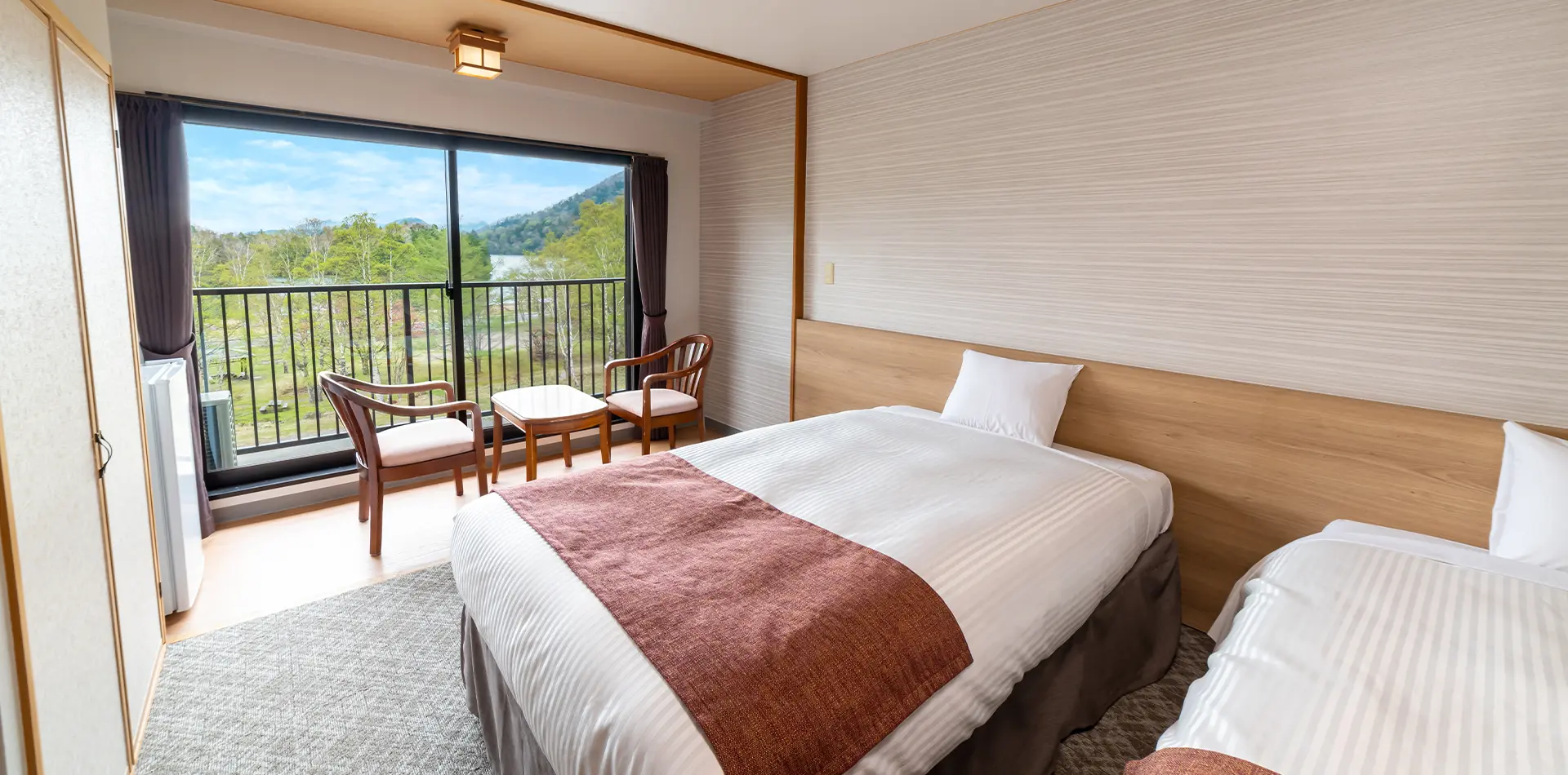 Twin-bed Japanese-Western guest room with armchairs and a balcony overlooking the Okunikko forest and lake