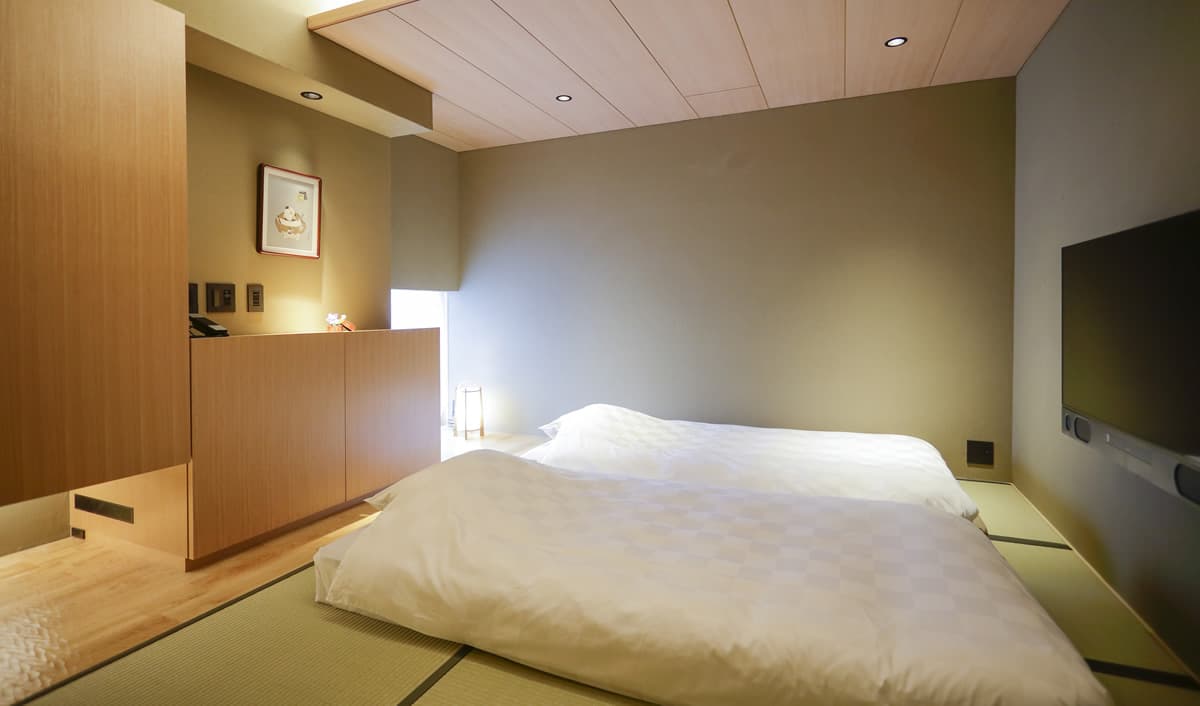 Tatami room with two futon beds laid out, wood-panelled ceiling and framed art at Kaminarimon Ryokan in Asakusa, Tokyo