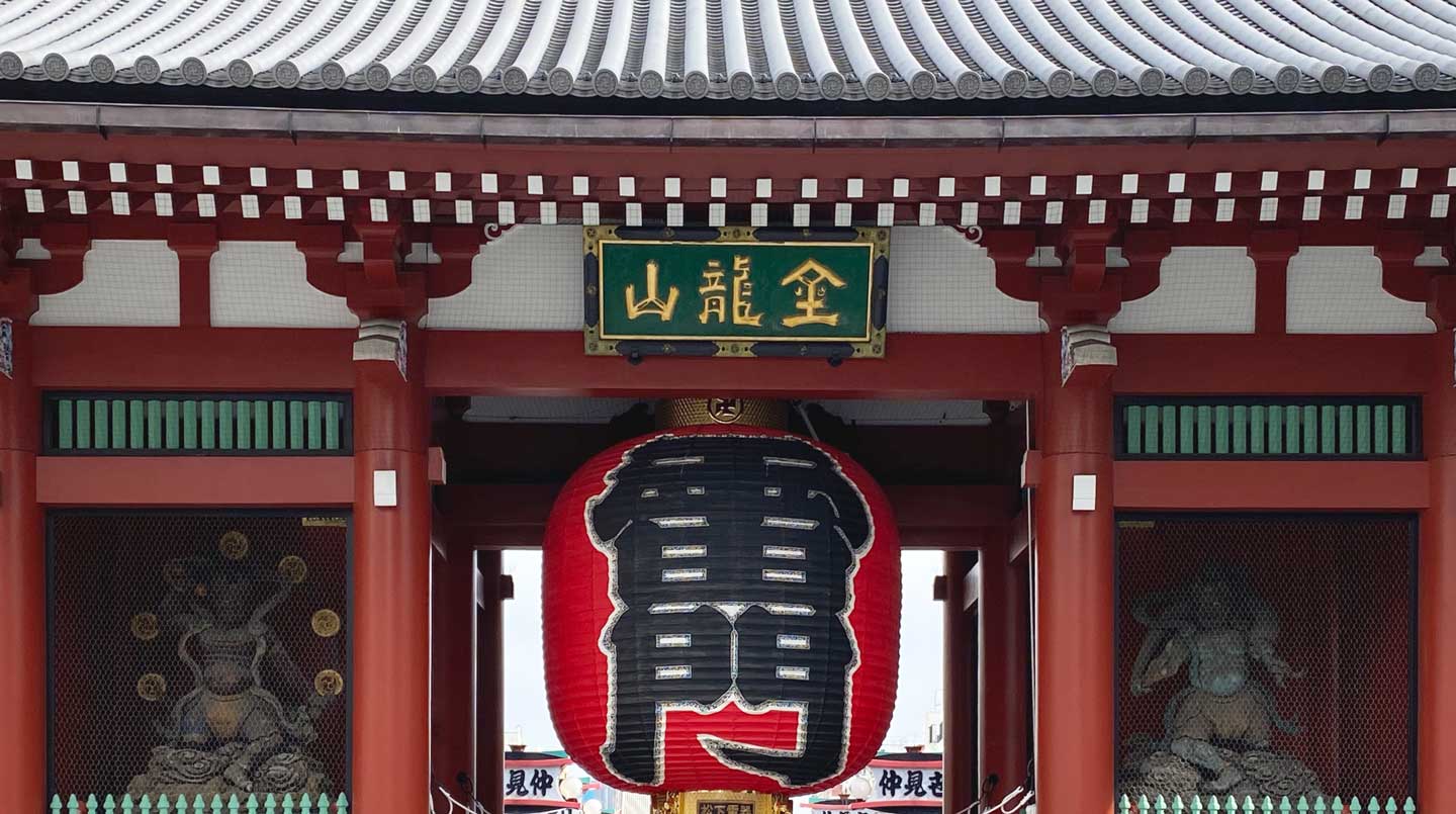 Close view of the gilded plaque and giant red lantern of Asakusa's Kaminarimon Gate, the namesake landmark of Kaminarimon Ryokan