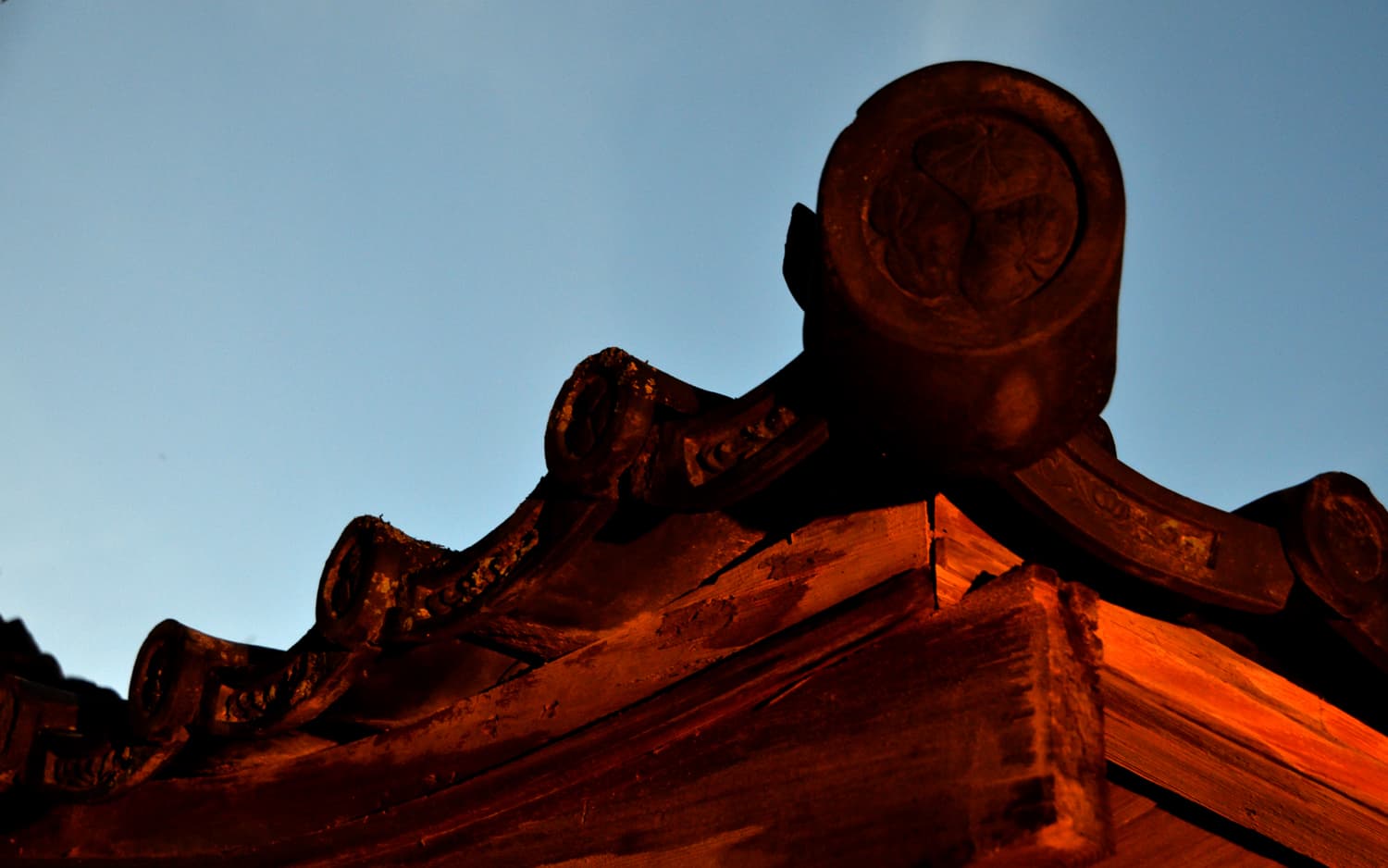 Close detail of a traditional crest-stamped roof end tile and timber eaves at Kankaso ryokan in Nara against a clear evening sky