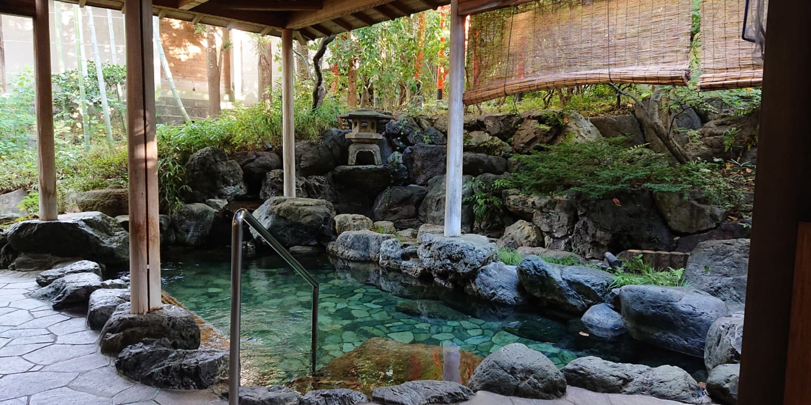 Outdoor rock rotenburo bath surrounded by a green garden and stone lantern at Kasuga Hotel in Nara