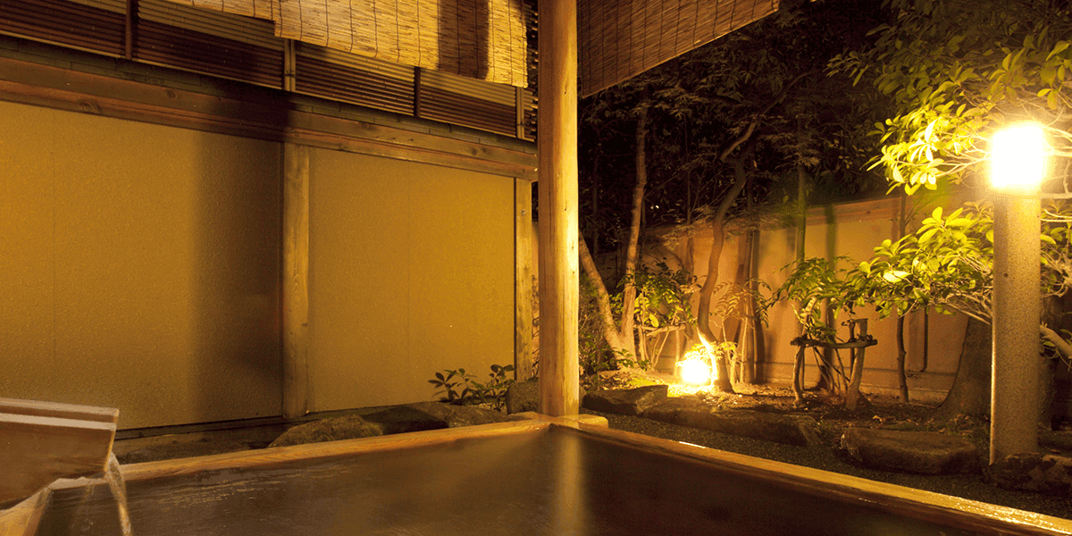 Stone open-air rotenburo bath with wooden bucket beside a softly lit night garden, Kawakamiya Kasuitei, Gero Onsen