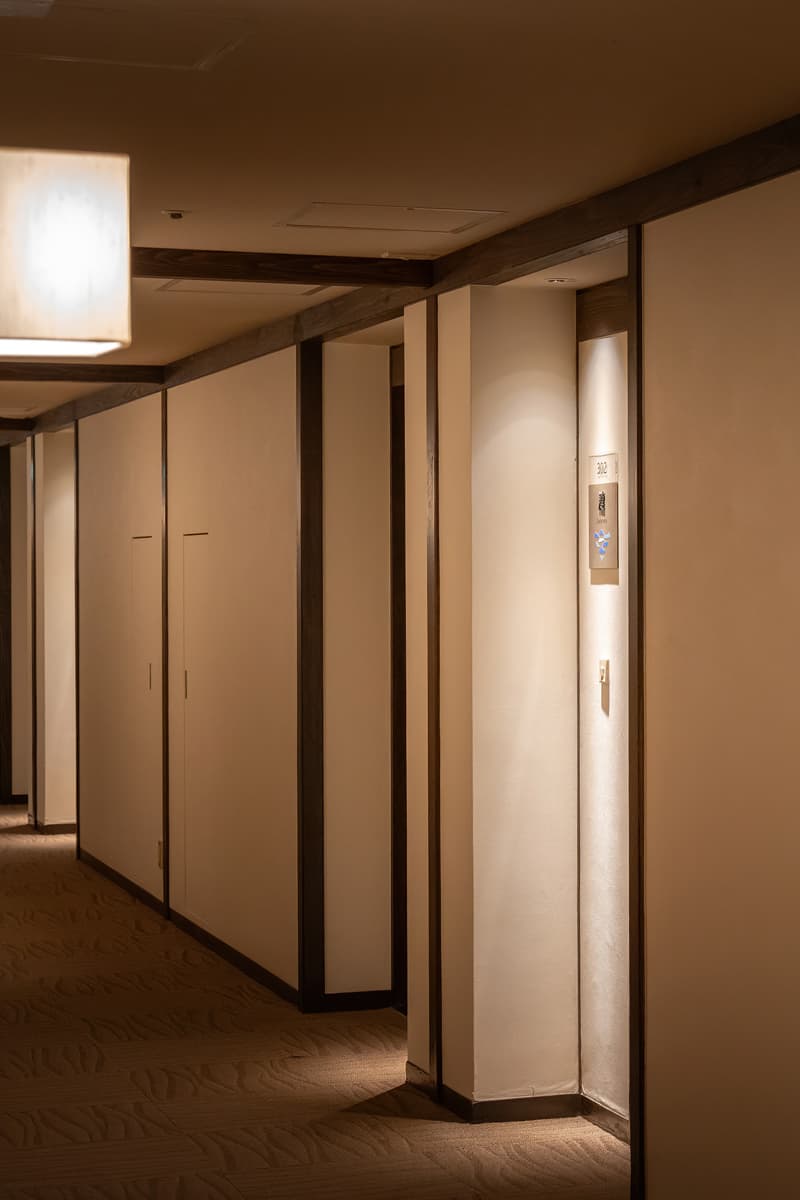 Guest-room corridor at Kinsuikan with washi room-number plaques, paper lantern and patterned carpet