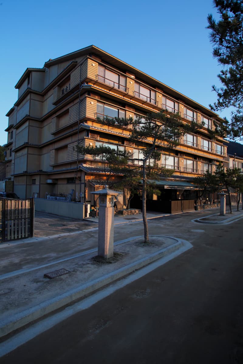 Kinsuikan ryokan full building exterior at dusk with a stone lantern and pine trees on Miyajima Island