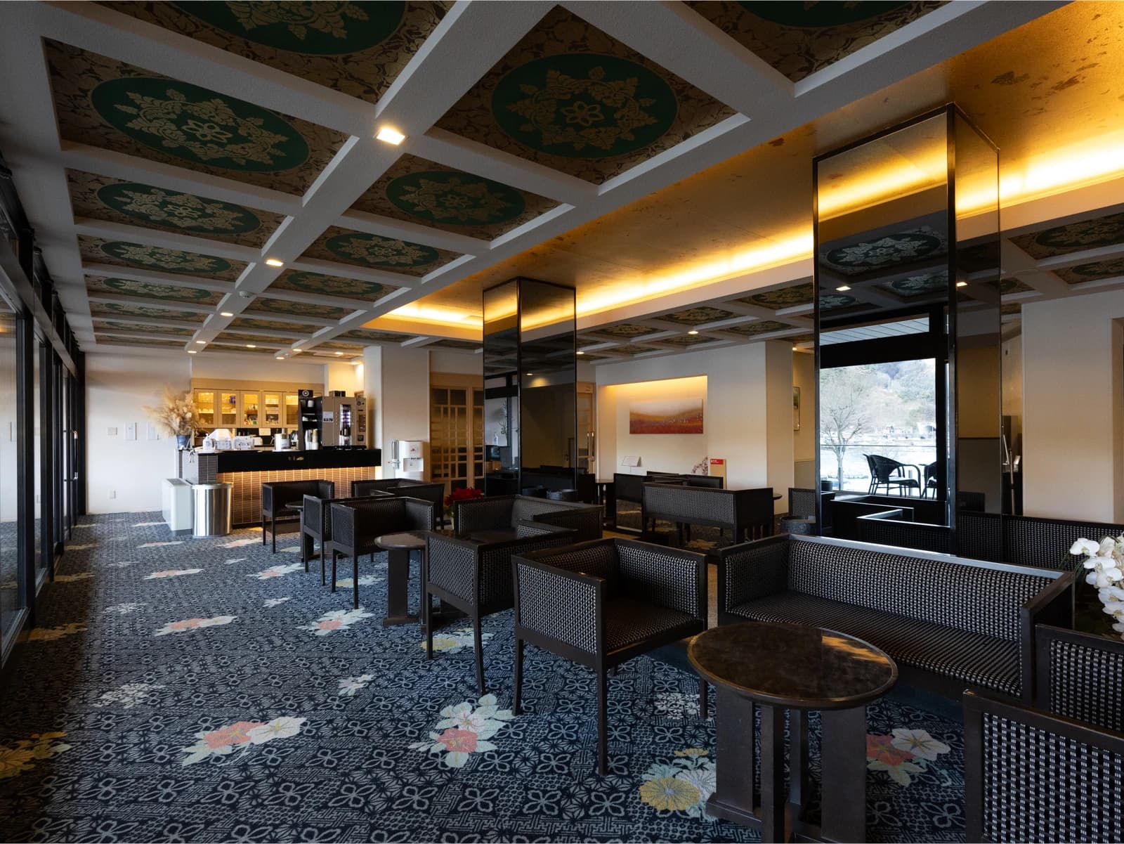 Lobby lounge at Konansou with a decorative green-and-gold coffered ceiling, patterned carpet, and seating by the lake-facing windows