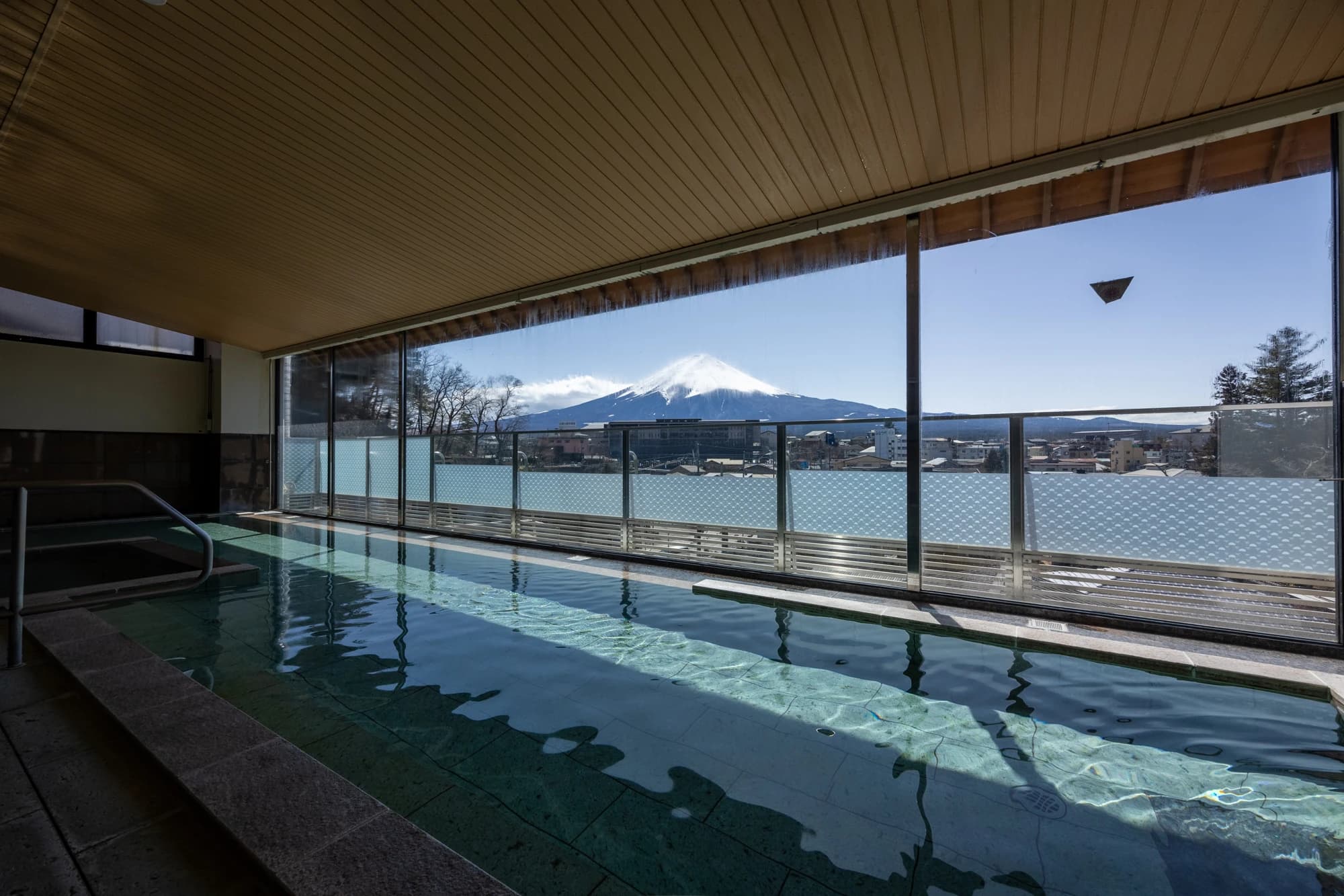Indoor hot-spring bath at Konansou with floor-to-ceiling windows framing a clear view of snow-capped Mt Fuji