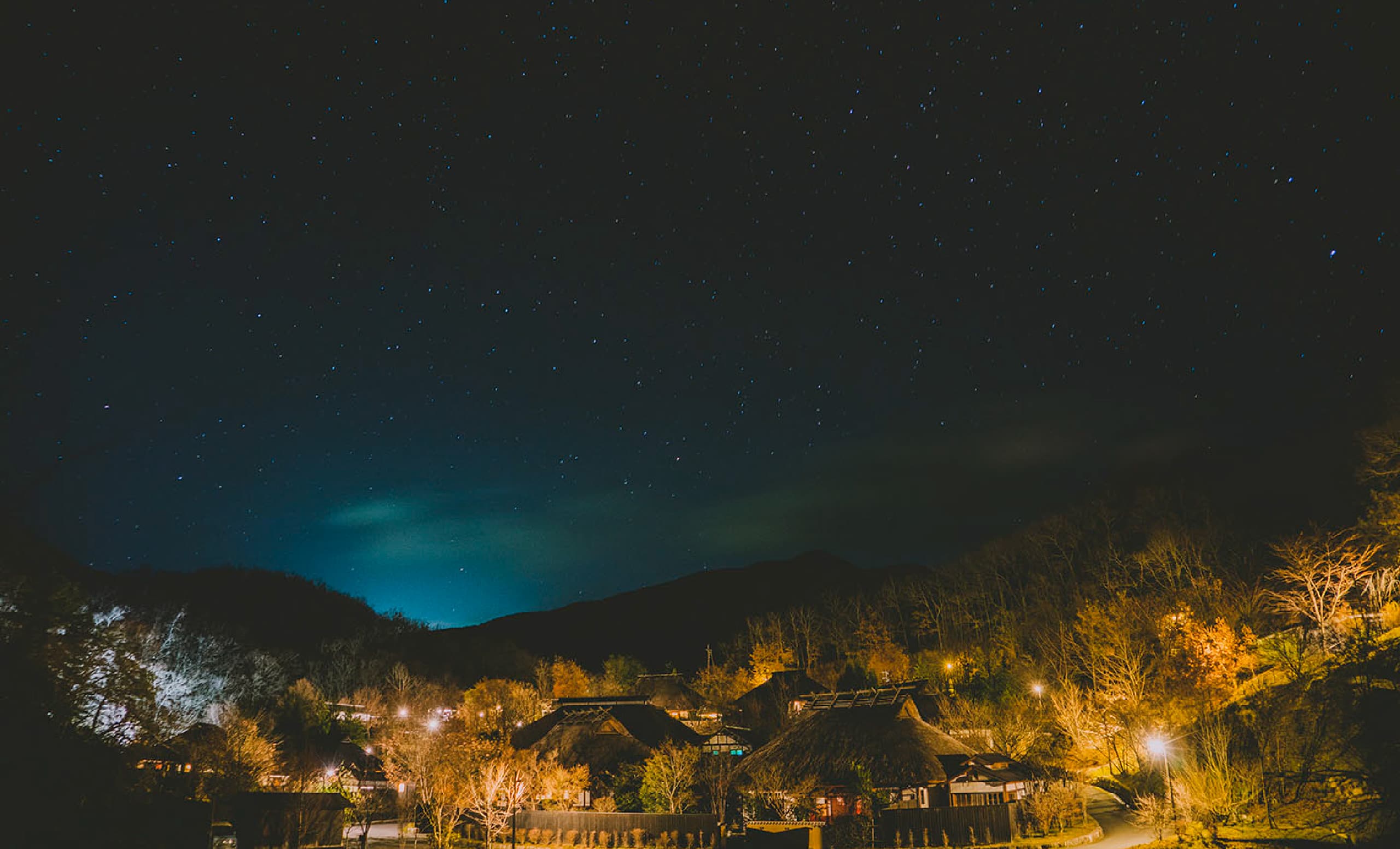 Yamamizuki Bettei Miyama Sansou thatched-roof buildings glowing beneath a starry night sky in the Kurokawa Onsen forest
