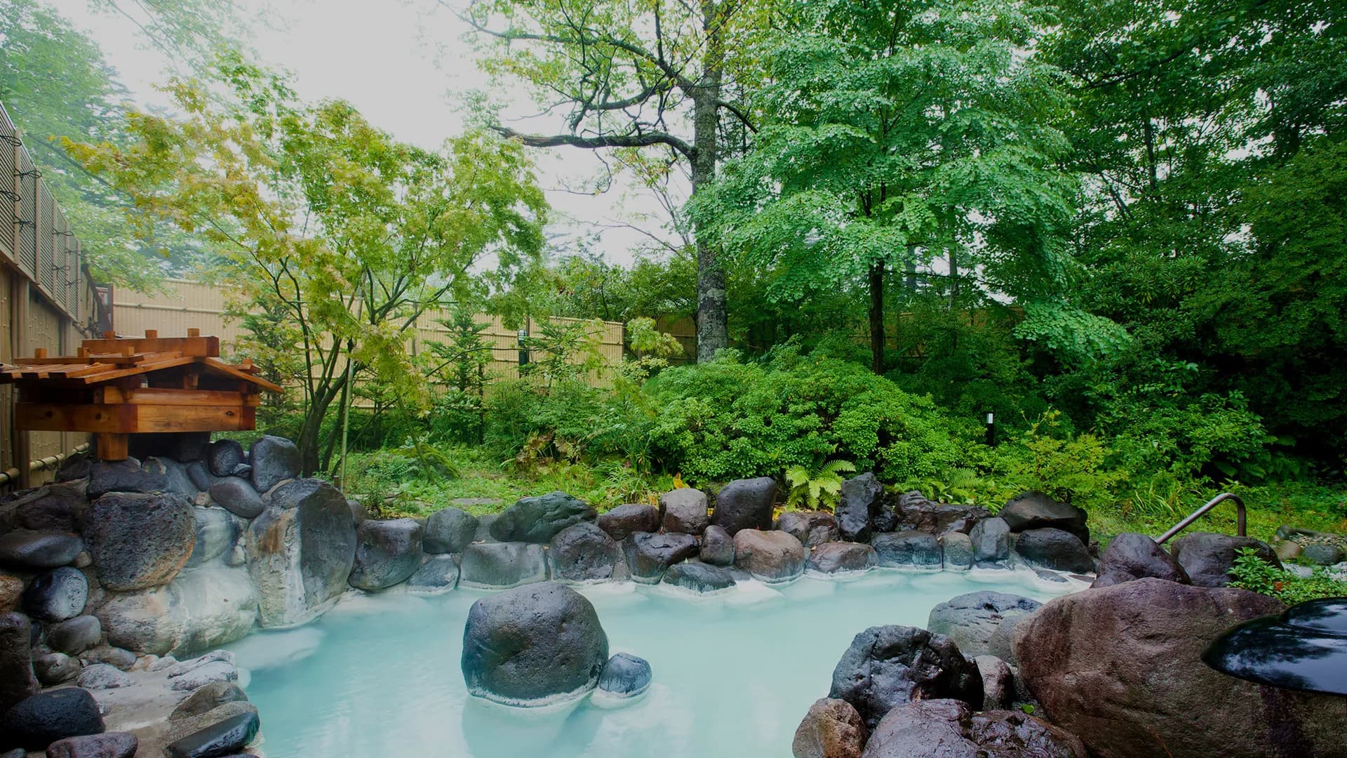Milky-blue open-air hot spring rotenburo ringed by mossy lava rocks and lush forest at Oku Nikko Mori no Hotel