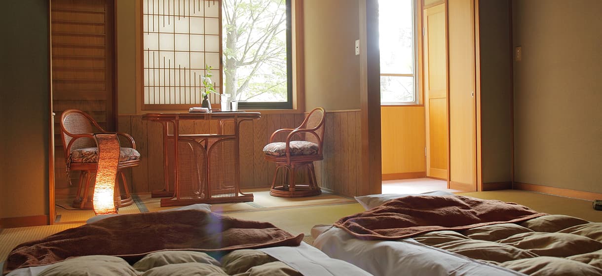 Tatami guest room at Morizuya with futon bedding made up and rattan chairs by a shoji window in evening light