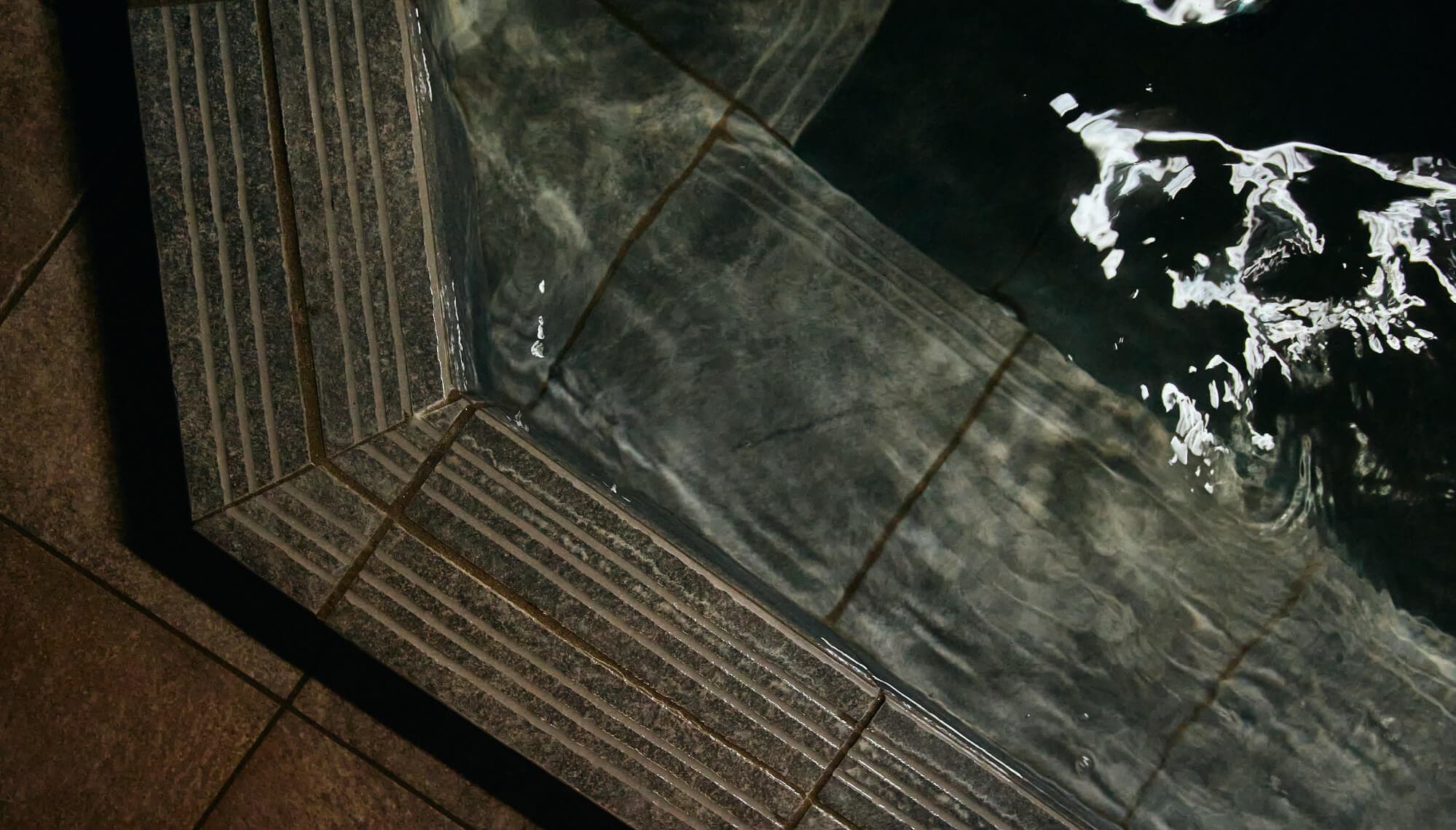 Close-up of the stone bath edge at Tsuchiya with dark mineral water and rippling reflections