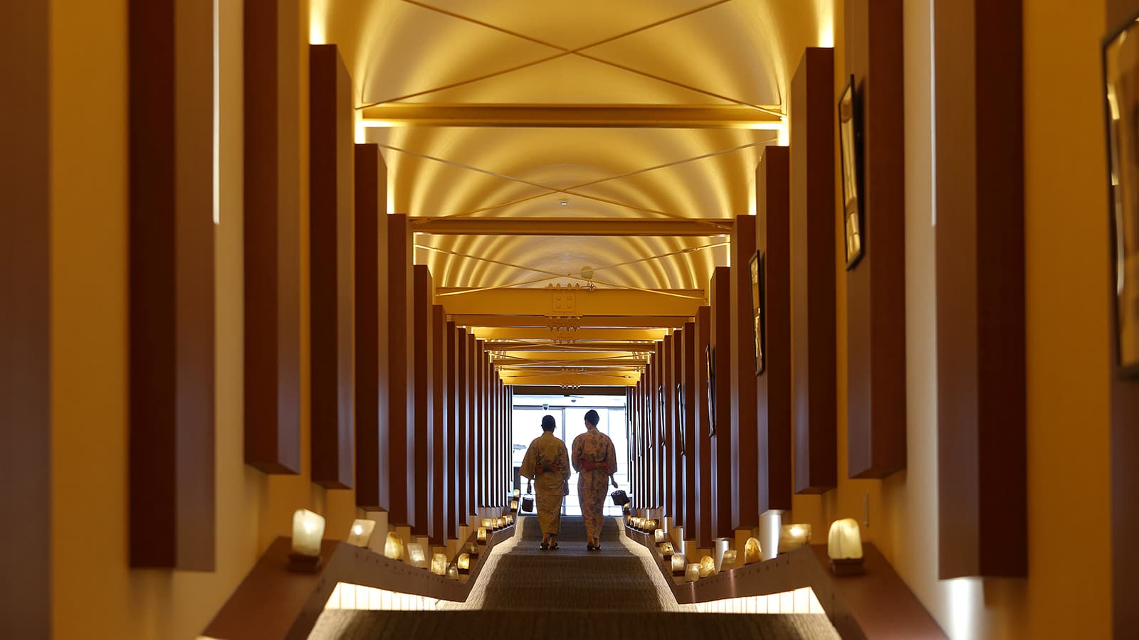 Long lantern-lit interior corridor with rhythmic wooden columns descending toward the lobby at Ryu Resort and Spa