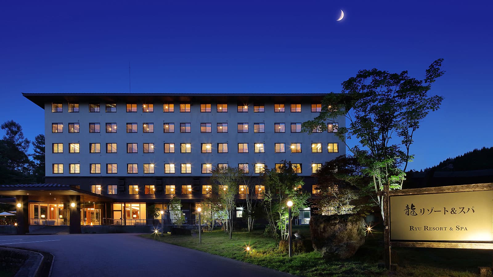Hotel Ryu Resort and Spa main building lit at dusk under a crescent moon, surrounded by forest near Takayama