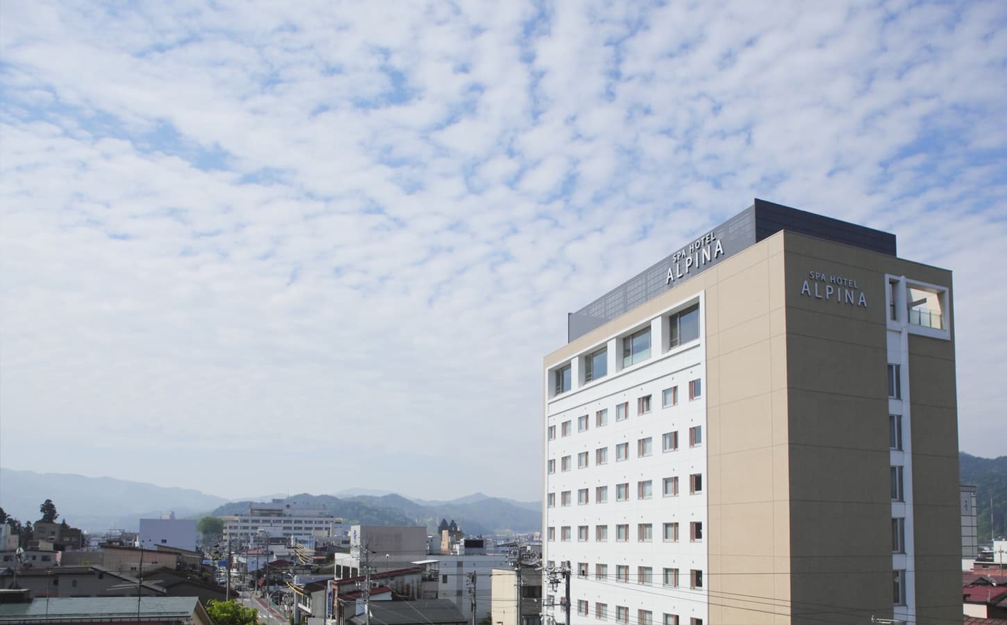 Spa Hotel Alpina Hida Takayama tall exterior with rooftop signage and the surrounding Hida town and mountains