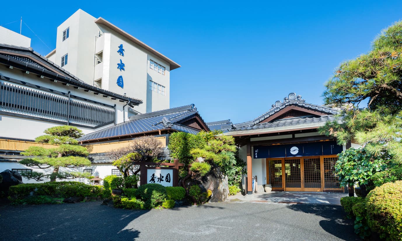 Daytime exterior of Ibusuki Shusuien with tiled-roof entrance gate and manicured pines, Ibusuki Onsen
