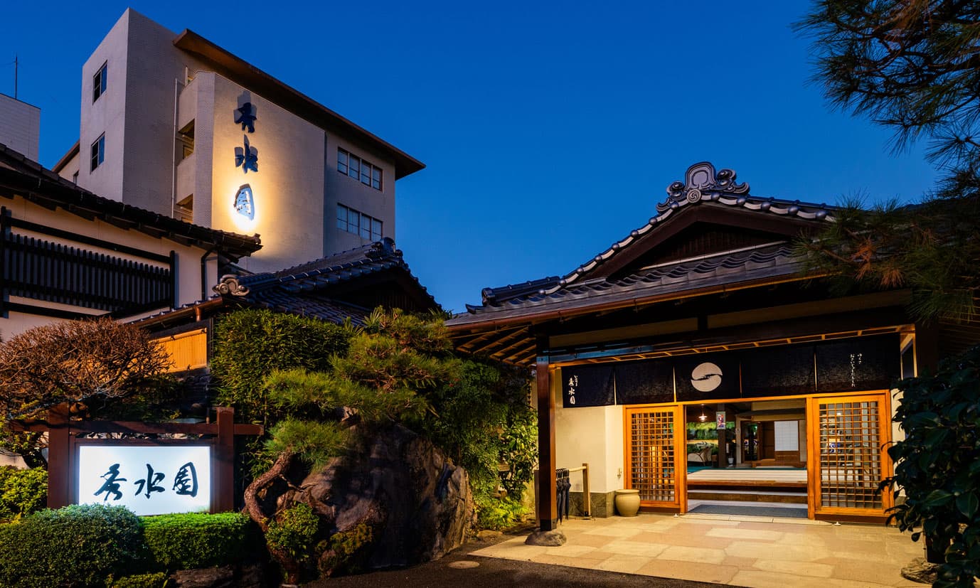 Ibusuki Shusuien ryokan entrance and tower wing illuminated at dusk with pine-framed stone garden, Ibusuki Onsen