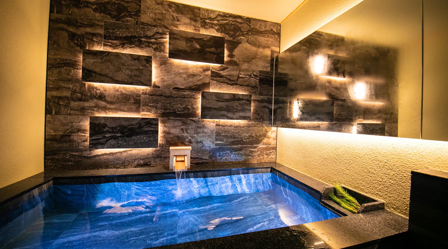 Private in-suite stone bath at Tokitotoki glowing blue against a layered slate accent wall