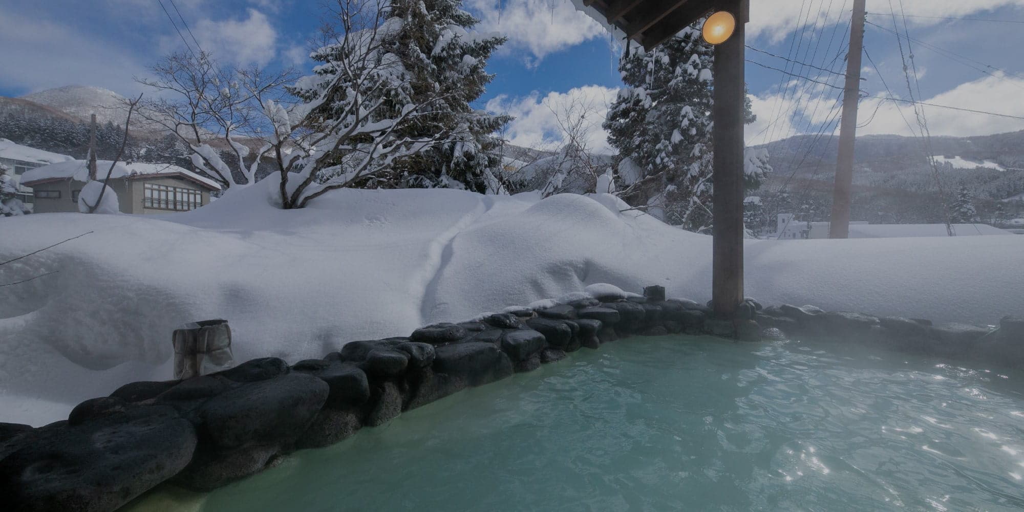 Outdoor rotenburo bath with milky sulfur water at Gokan no Yu Tsuruya, ringed by deep snow and the Zao Onsen mountains