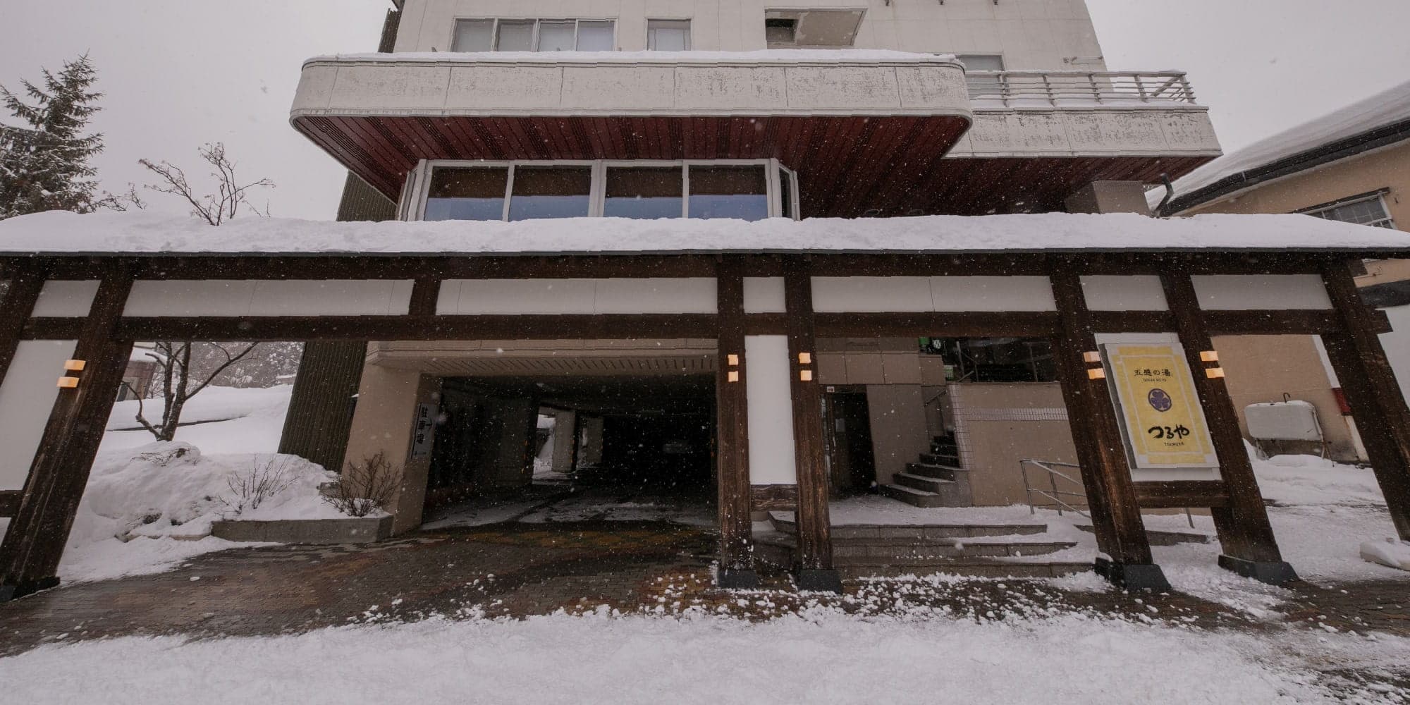 Snow-covered entrance and timber porte-cochere of Gokan no Yu Tsuruya in Zao Onsen during winter