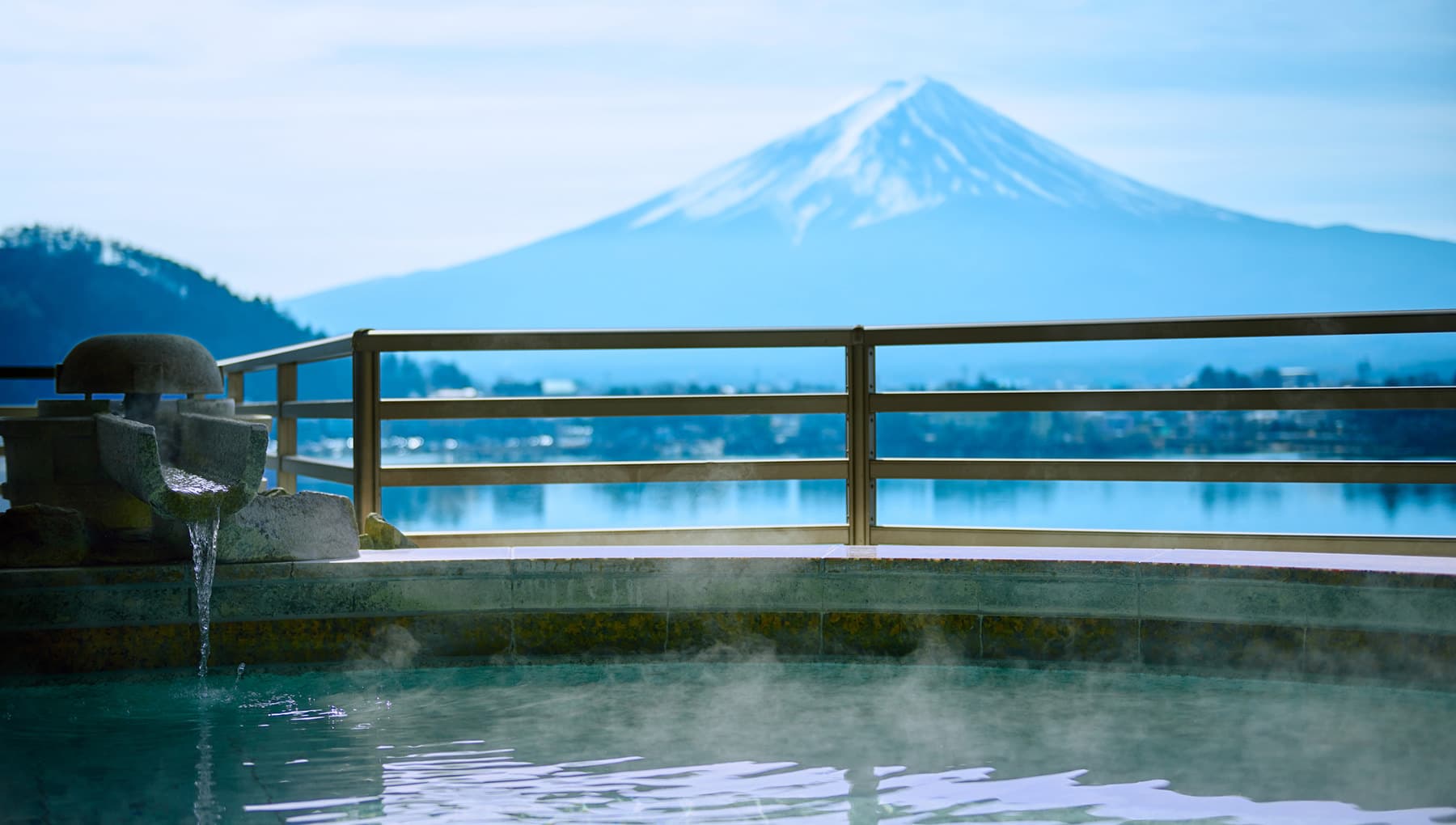 Open-air rotenburo bath at Kozantei Ubuya with rising steam and a clear view of Mt. Fuji across Lake Kawaguchiko