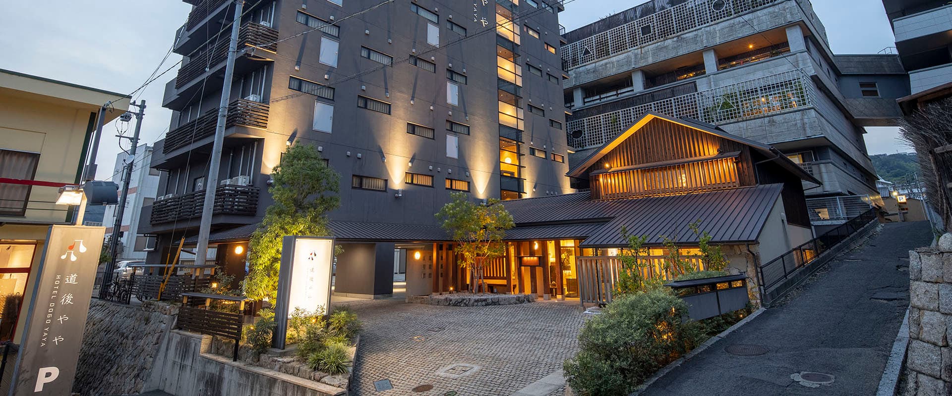 Hotel Dogo Yaya exterior at dusk with warmly lit entrance and modern facade in Dogo Onsen, Matsuyama