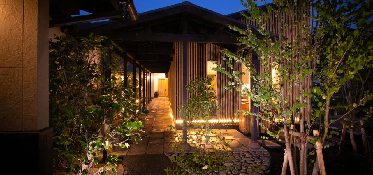 Lantern-lit stone entrance path leading to the wood-clad guest villas at Oyado Den Rikyu at dusk