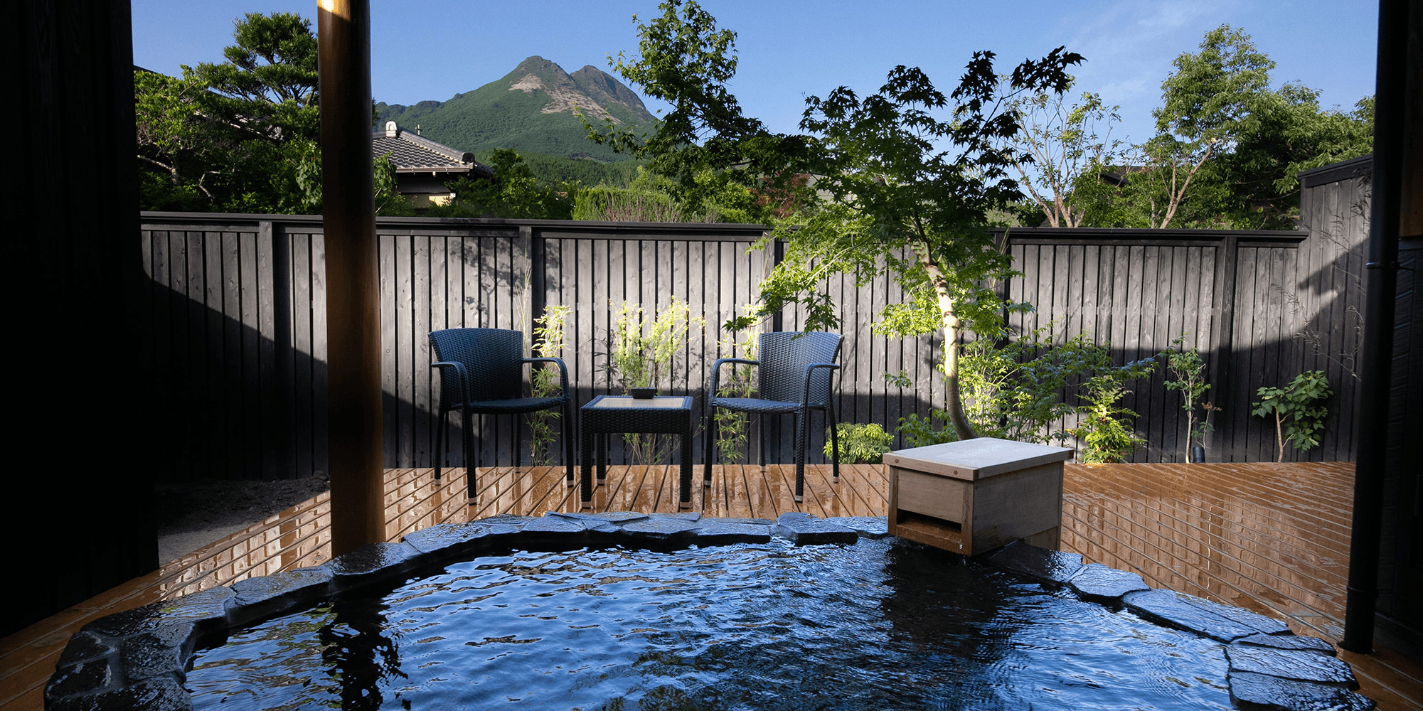 Private open-air bath at Oyado Den Rikyu in Yufuin onsen, with a clear view of Mt. Yufu beyond a wooden fence