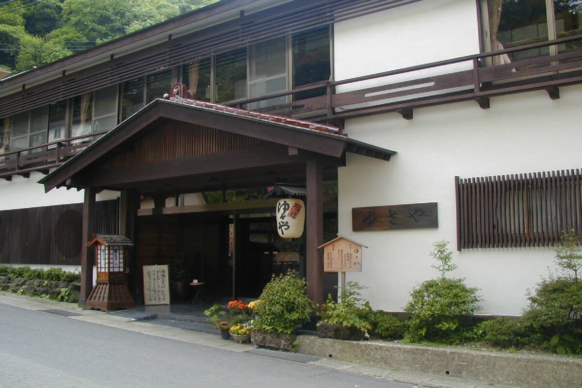 Daytime exterior of Yusaya Ryokan's traditional white-walled main building and wooden entrance porch in Naruko Onsen