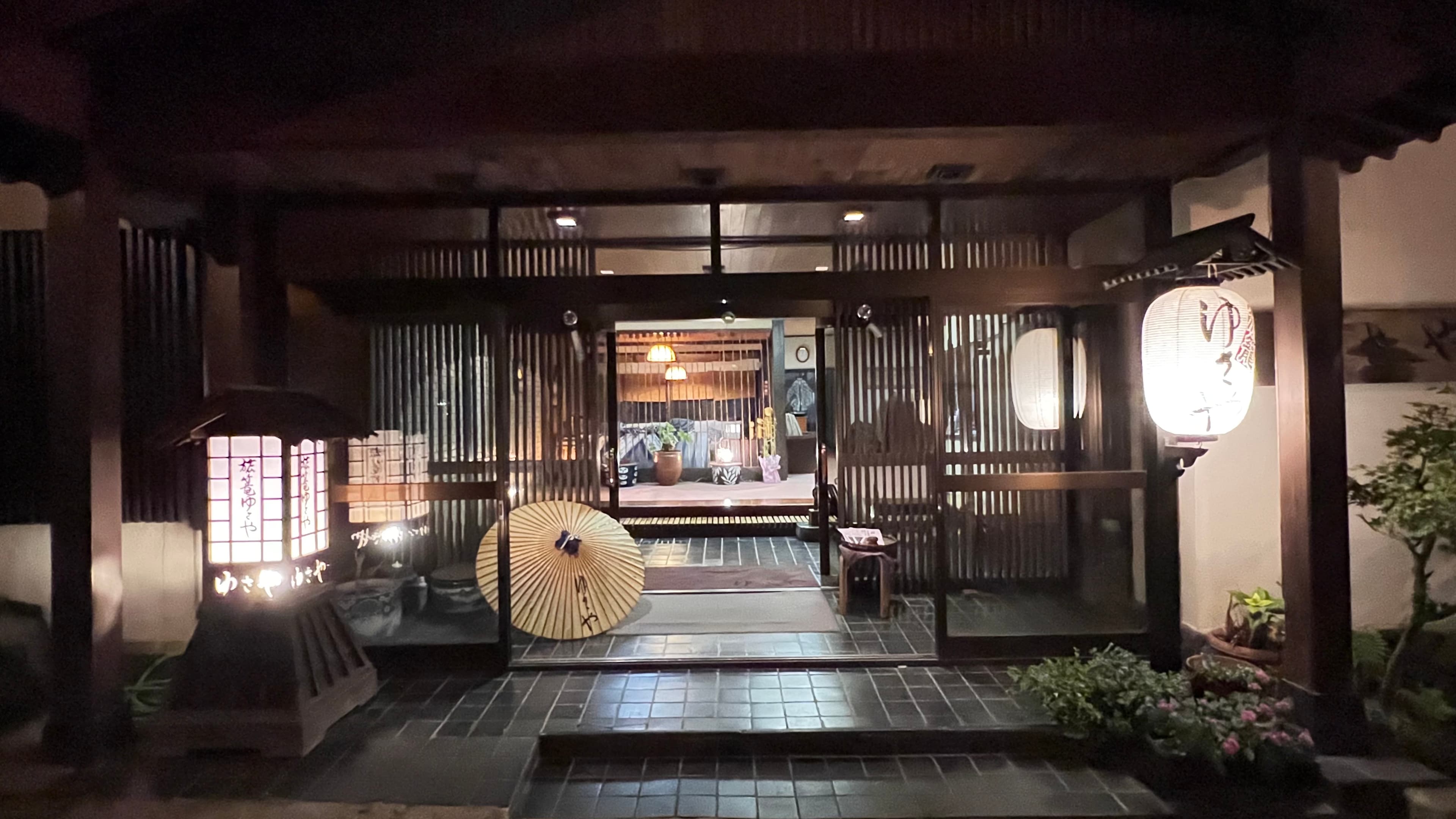 Yusaya Ryokan illuminated wooden entrance at night with paper lanterns and a wagasa umbrella, Naruko Onsen, Miyagi