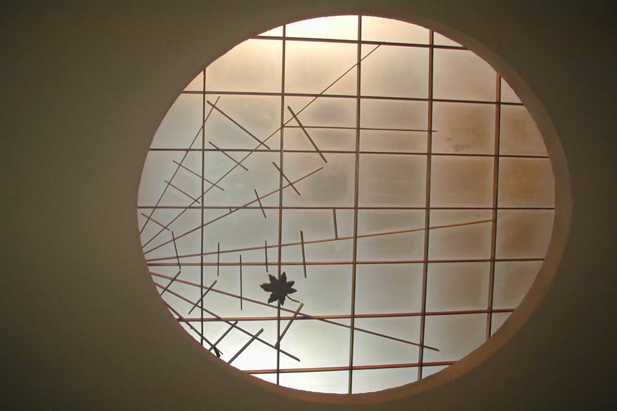 Round latticed window detail at Yusaya Ryokan with a single maple leaf motif, soft natural backlight