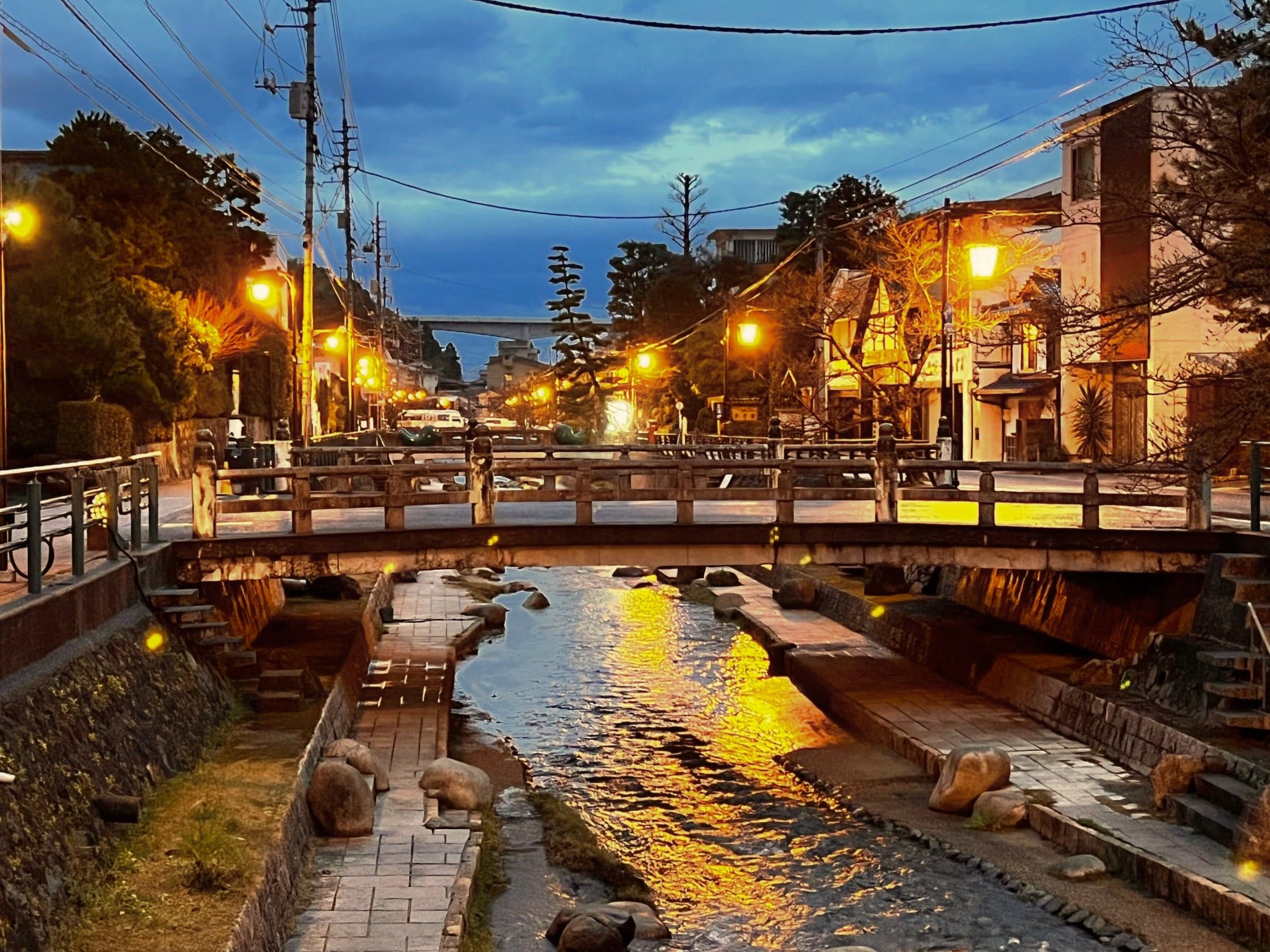 Tamatsukuri Onsen canal and arched bridge lit by lanterns at dusk near Yumoto Tamaikan, Shimane